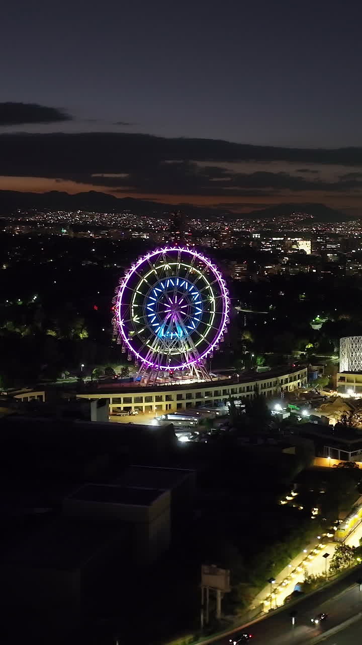 Vertical aerial view orbiting the ferris wheel of Aztlan Park, night in CMDX
