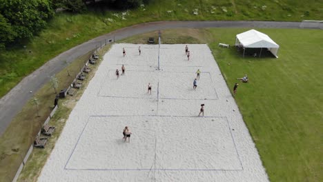 aéreo: tiro de dron de voleibol de playa entre un paisaje exuberante con árboles verdes mientras la gente juega voleibol de playa en la arena