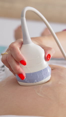 ultrasound scan to a pregnant woman in hospital. gynecologist using transducer on female's belly during sonography procedure. vertical video