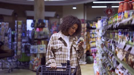 Hübsche-Frau,-Die-Mit-Einem-Einkaufswagen-Durch-Den-Gang-Im-Supermarkt-Läuft-Und-Die-Regale-Betrachtet