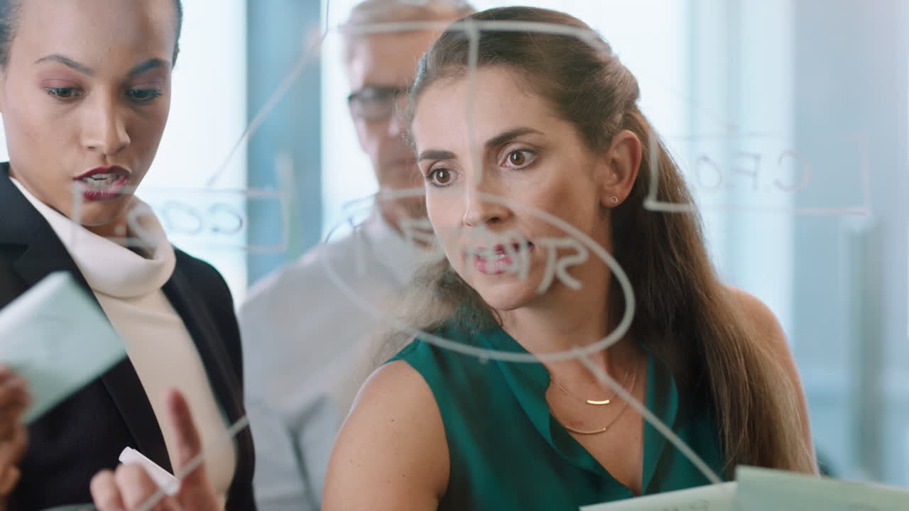 business team meeting using sticky notes writing on glass whiteboard brainstorming colleagues working on problem solving strategy thinking of solution for project in office through glass