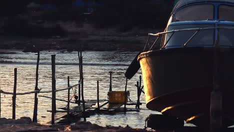 close shot of the front of a boat on the shore in the evening time with boats going past behind it on the lake, in front of shoreline