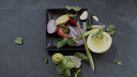 coriander falling like snow onto plate of ingredients - raw onion, strawberry, wasabi, ginger, lemon and asparagus