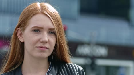 a beautiful optimistic redhead woman looks at the camera and smiles sweetly in the city