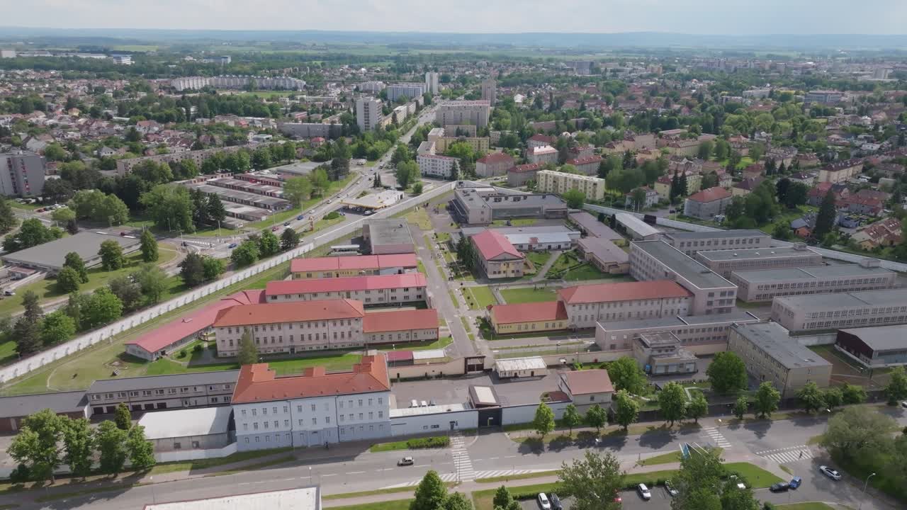 Aerial wide-to-medium push-in toward the prison entrance gate and security checkpoint; steady forward motion, continuous shot, daytime