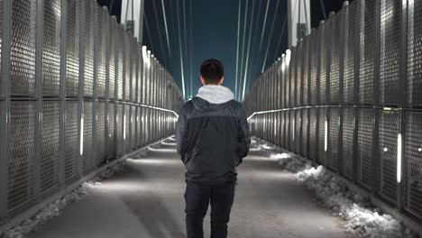 young white male walking away from camera on a pedestrian bridge at night