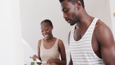 Happy-african-american-couple-brushing-teeth-together-and-talking-in-bathroom,-in-slow-motion