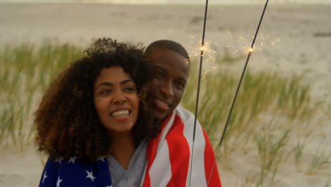 Front-view-of-African-american-couple-holding-sparklers-in-hands-at-beach-4k