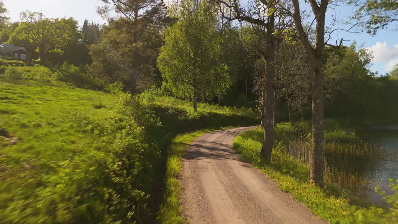 Vista aerea che segue una strada sterrata tortuosa lungo la riva del lago Teåkersjön attraverso lo scenografico paesaggio rurale di Dalskog vicino a Mellerud, con foreste, riflessi sull'acqua e paesaggio rurale svedese