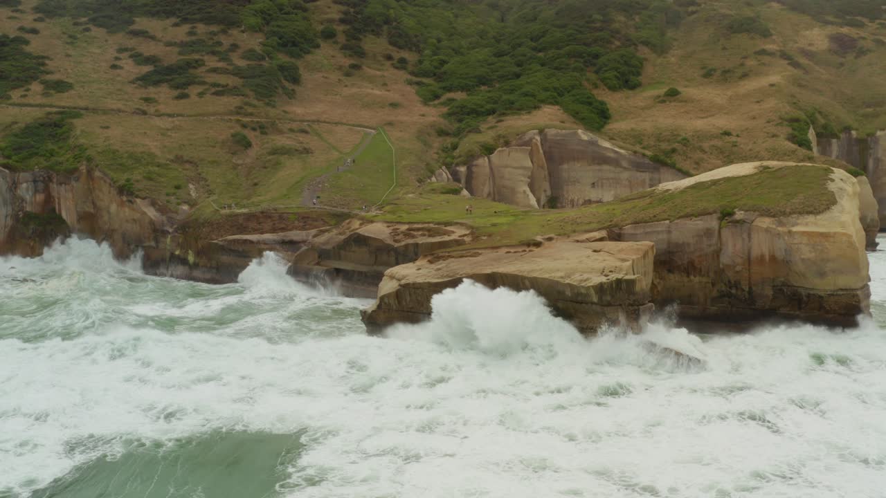 toma aérea de sobrevuelo de olas rompiendo contra las paredes de los acantilados a lo largo de la costa en nueva zelanda durante las horas del atardecer