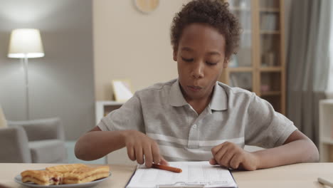 child eating sandwich and doing homework