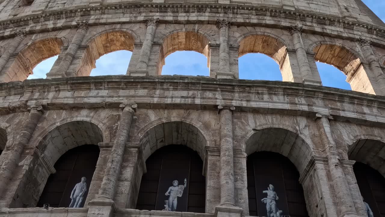 Close-up of the Colosseum's arches featuring statues and architectural details under a clear sky.