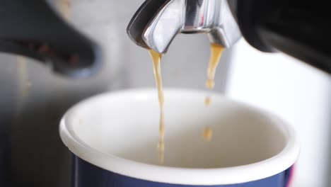 movimiento lento cerca hacia abajo ángulo de espresso marrón rico vertiendo fuera de la máquina de espresso en taza azul