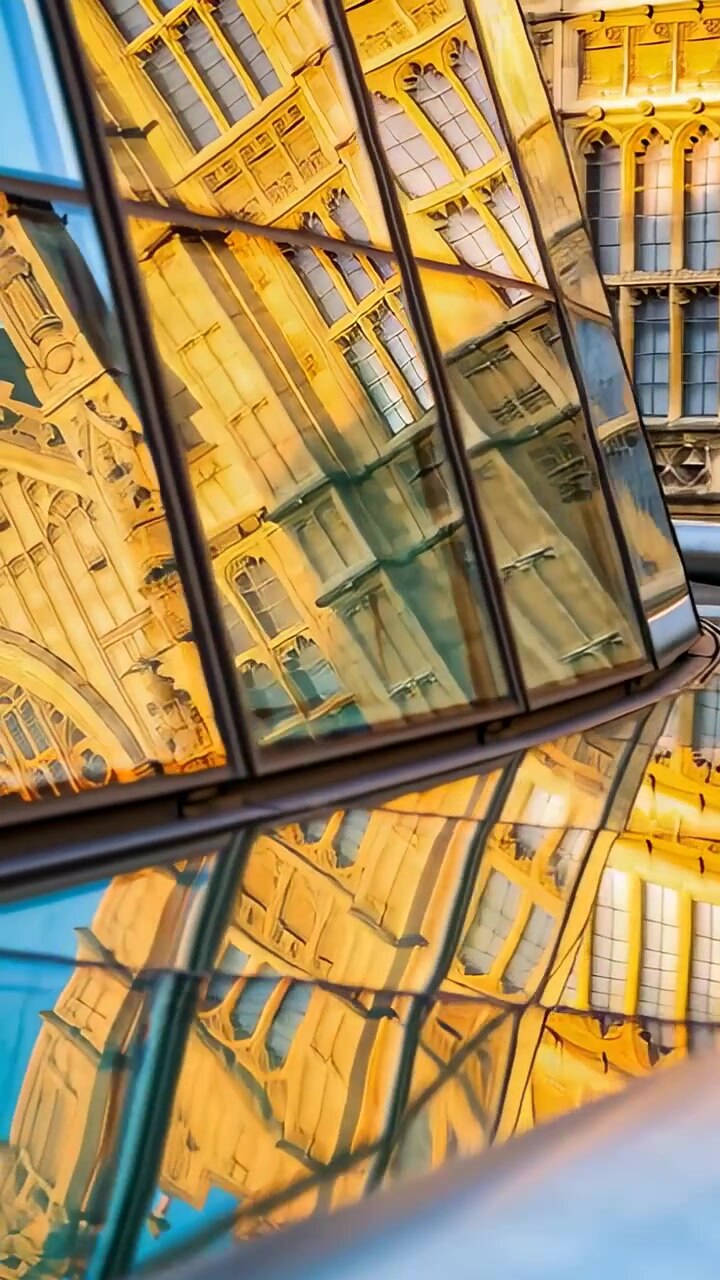 Video vertical: Cámara inclinándose, fachada de cristal curvado que refleja en una plaza, mostrando parteluces y molduras metálicas.