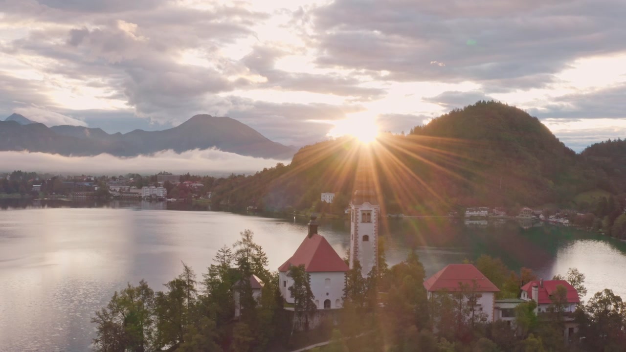 Tramonto dorato sulle montagne, sul Lago di Bled e la Chiesa di pellegrinaggio dell'Assunzione di Maria in Slovenia. Ripresa aerea con drone.