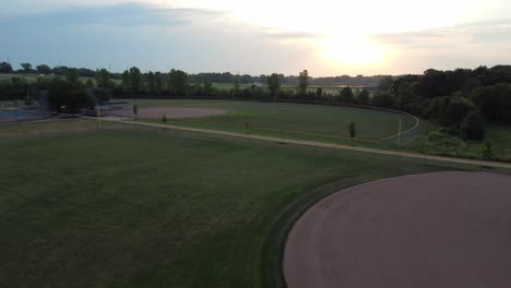 Imágenes-De-Drones-Subiendo-O-Movimiento-De-Grúa-Sobre-Un-Campo-De-Diamantes-De-Béisbol-Con-Un-Amanecer-En-El-Fondo