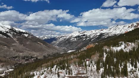 Aerial-View-of-Snowcapped-Mountains-with-Pine-Trees-in-the-foreground,-Drone-slowly-panning-around-trees,-partial-blue-skies-with-a-few-clouds,-San-Juan-Mountains,-Ironton-Colorado,-establishing-shot