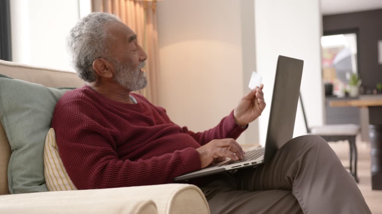 Happy senior biracial man using laptop for online shopping, unaltered, in slow motion