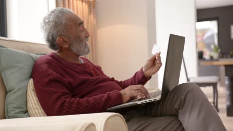 Happy-senior-biracial-man-using-laptop-for-online-shopping,-unaltered,-in-slow-motion