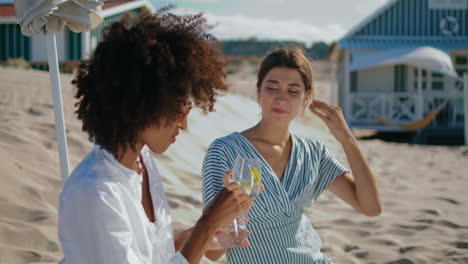 happy girlfriends drinking picnic cocktails at beach houses. smiling lgbt couple