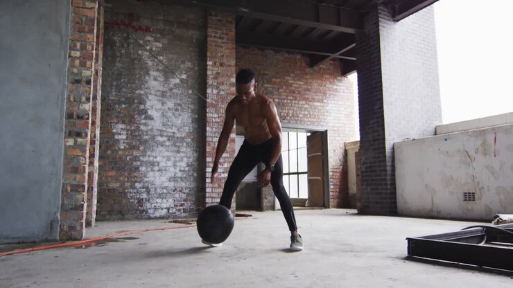 Shirtless african american man exercising with medicine ball in an empty urban building