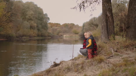 young mother is showing to her little son lake and forest walking at nature at autumn day happy motherhood and childhood family rest at weekend