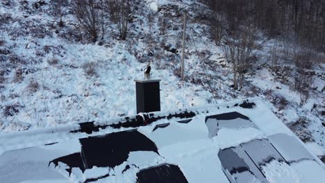 smoke coming from wood stove chimney while moving bacwards to reveal snow covered solar roof and frozen landscape - norway winter season aerial