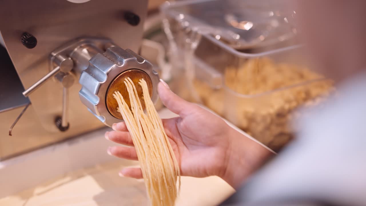 남성 요리사는 파스타 기계에서 스파게티의 긴 가닥을 동반