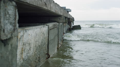 Waves-crashing-urban-bridge-in-sea-coastline-on-cloudy-weather.-Sadness-concept.