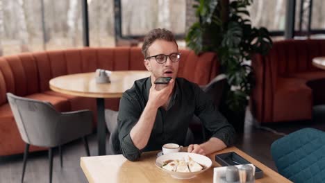 Hombre-Guapo-En-Un-Café-Hablando-En-Un-Chat-De-Voz-A-Través-De-Un-Teléfono-Inteligente