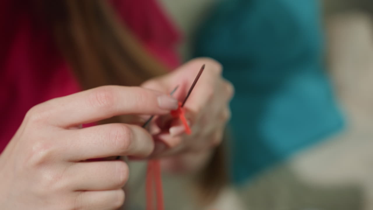 차분하게 붉은색 실과 금속 바늘, 양모 텍스처를 사용하여 손으로 바느질하는 모습이에요. 붉은색 실과 금속 바늘로 정성스럽게 바느질하는 손을 평화로운 클로즈업 화면으로 보여줍니다.