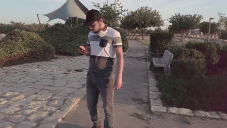 young man, checks his mobile, walking through a public park