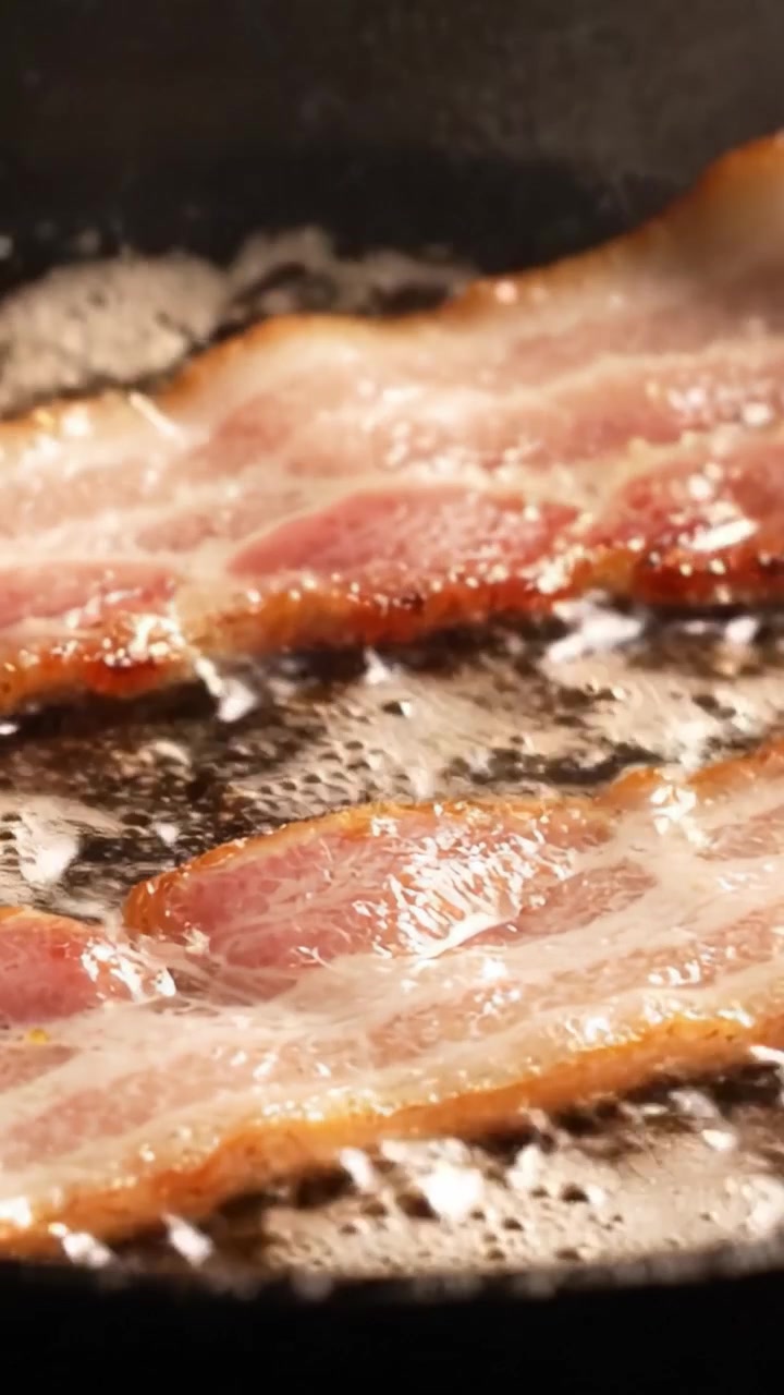 Sprødt bacon, der syder på en pande: En nærbillede-rejse af perfekt tilberedt bacon, der fremhæver den saftige tekstur og den smagfulde aroma af stegt kød.
