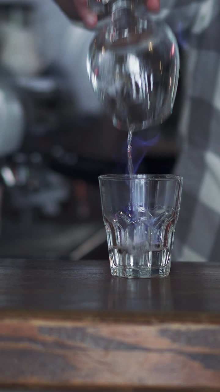 Beautiful motion shot of professional barista making cocktail with two glasses at the bar. Bartender burning Sambuca. Vertical video.