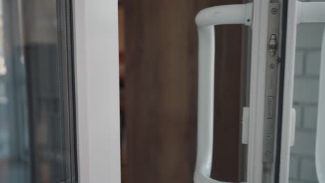 close up of person in black leather jacket stepping out from store while another enters, both holding door handles, automatic glass door slowly closes by itself with soft lighting in modern entryway