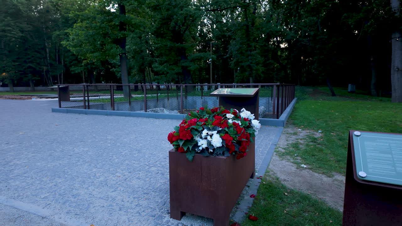 The Soldiers' Cemetery at Westerplatte featuring a planter box with red and white flowers and commemorative information boards in the dark park