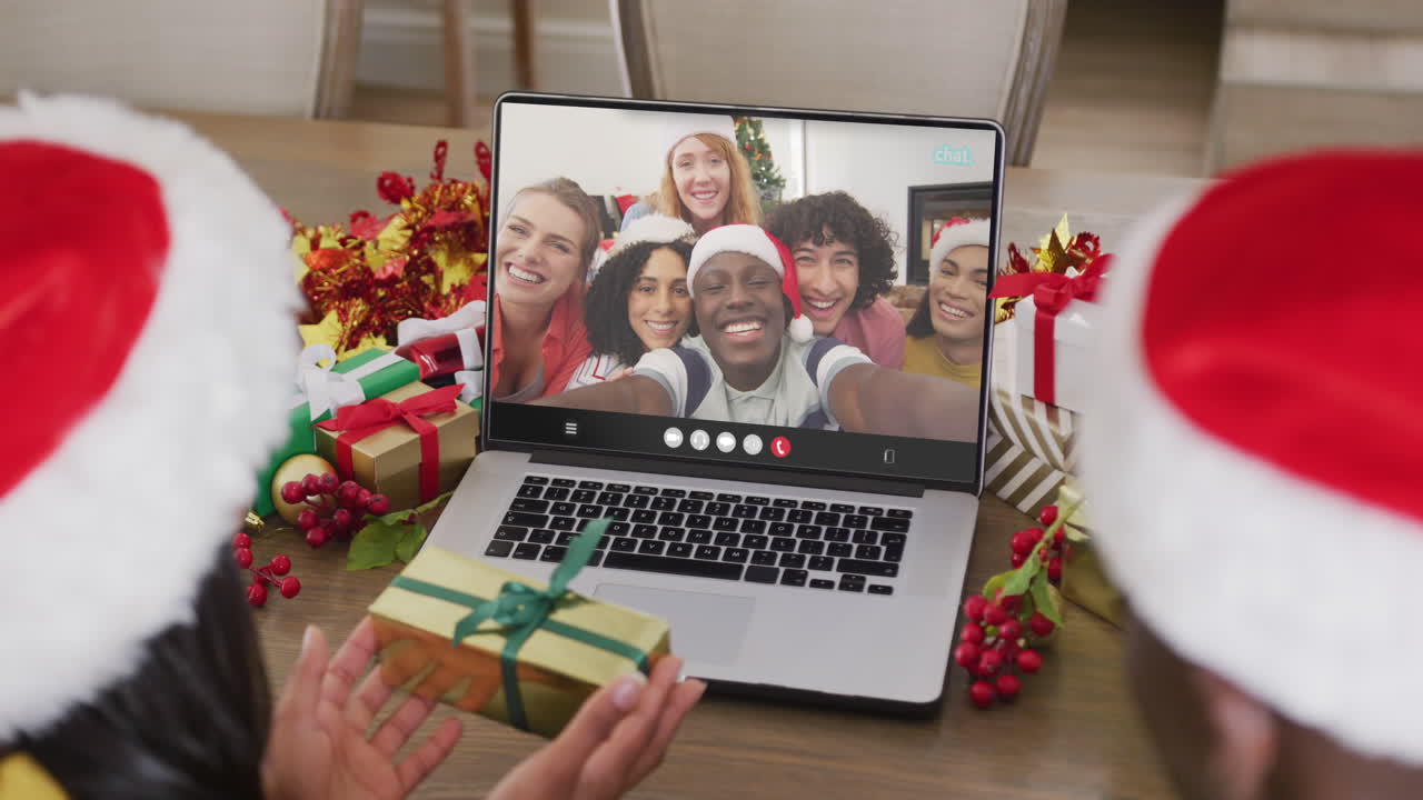 pareja diversa con sombreros de santa teniendo llamada de video portátil con amigos diversos