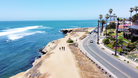 Car-driving-through-luxury-coastal-house-area-with-rocky-cliff,-aerial-view