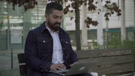 hombre barbudo trabajando con una computadora portátil enfocado al aire libre