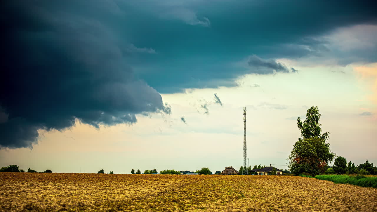 Stormy clouds above farmland fields and a cellular tower in the countryside - time lapse
