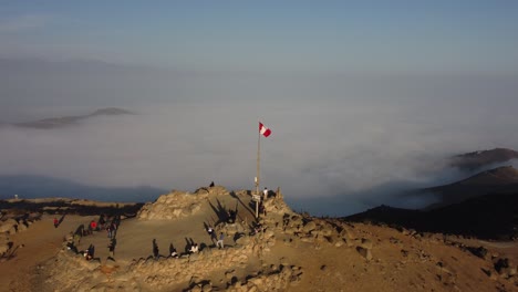 peruvian flag on top of a mountain that rises above the clouds