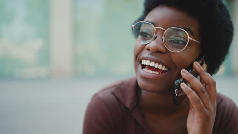 Close-up-African-girl-in-glasses-smiling-talking-over-mobile-phone-outdoors