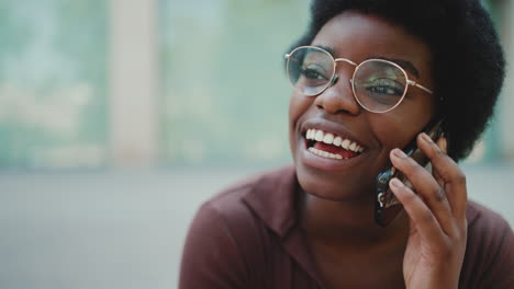 close up african girl in glasses smiling talking over mobile phone outdoors