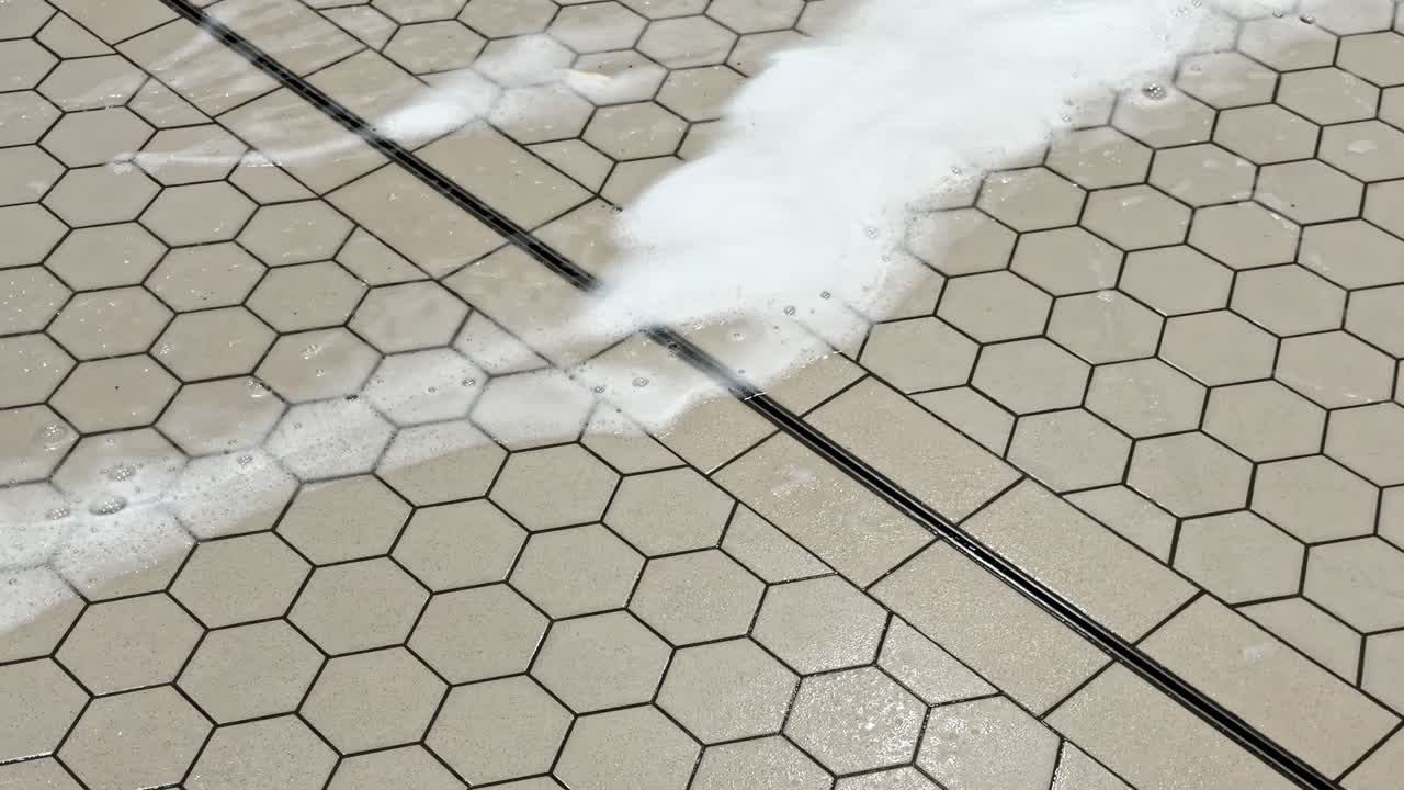 Foam and water being pushed across a tiled floor with a squeegee during an industrial washdown, highlighting sanitation workflow