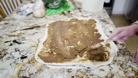 extendiendo las especias de canela y azúcar moreno en la masa para enrollar en bollos de canela
