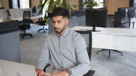 using smartphone, indian man checking messages while sitting in modern office