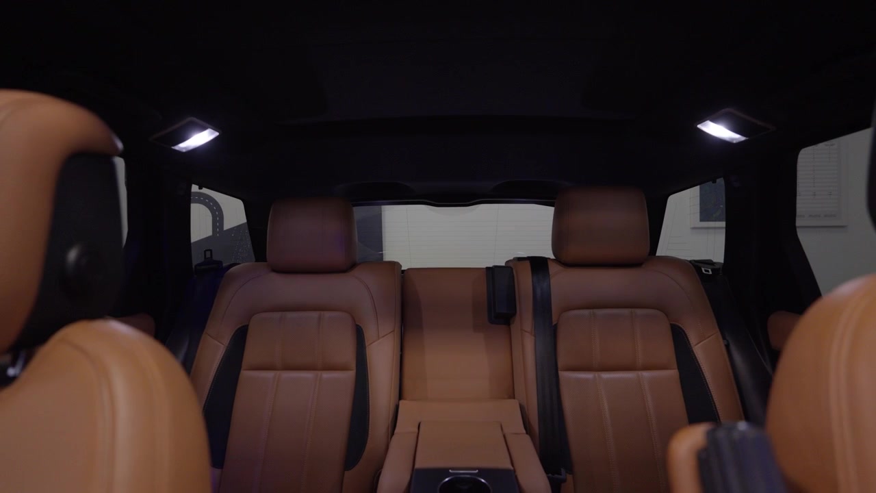 Interior de coche de lujo mostrando el habitáculo de pasajeros con cuatro asientos de cuero marrón premium. Luces LED blancas brillantes iluminando el espacio.