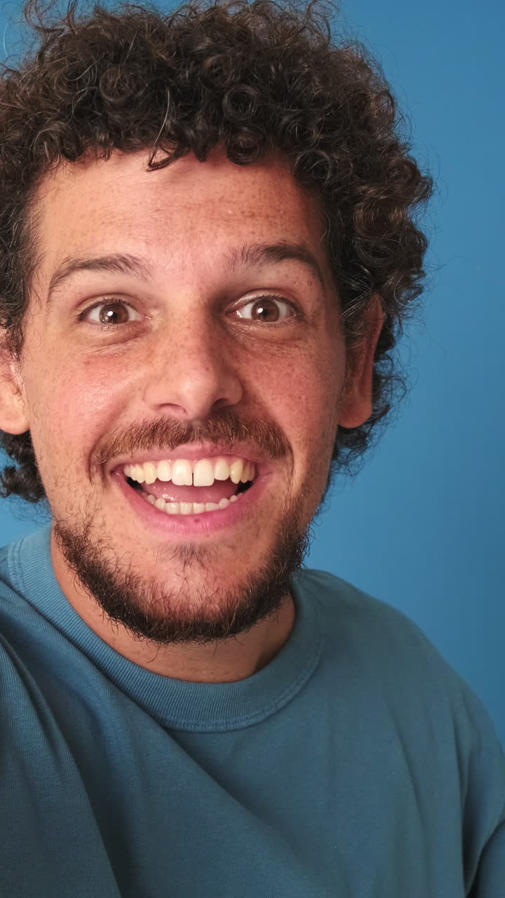 Joven expresivo hablando, sonriendo y saludando sobre un fondo azul