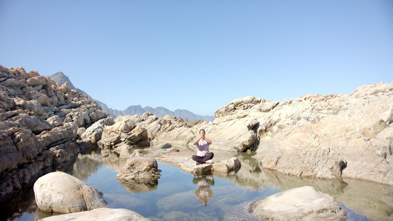 Meditating on rock, woman practicing yoga in serene mountain landscape