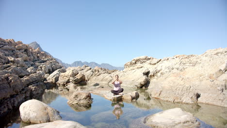 meditating on rock, woman practicing yoga in serene mountain landscape